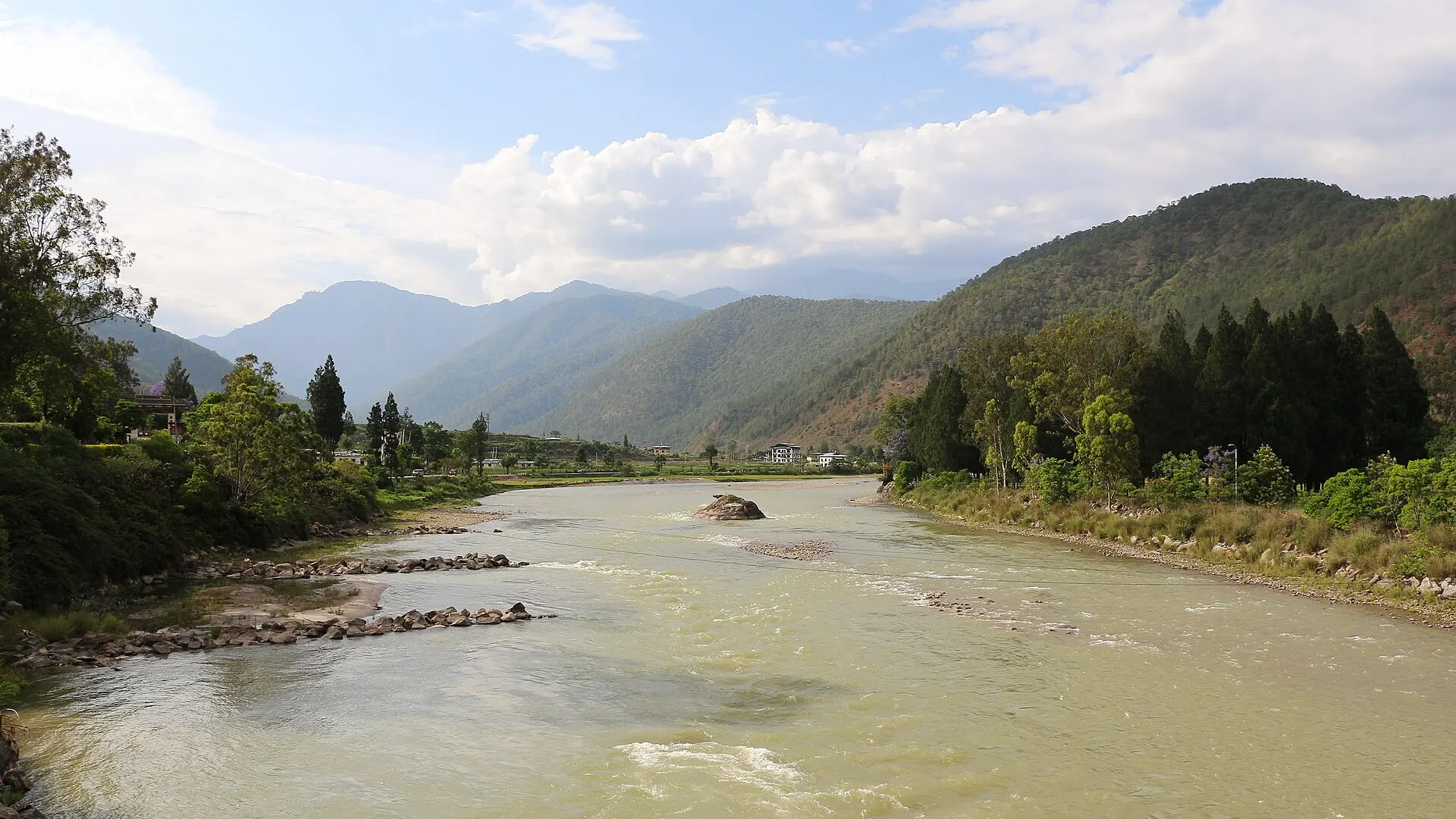 The Mo Chhu river flowing between wooded hills past riverside fields and scattered buildings near Punakha in western Bhutan
