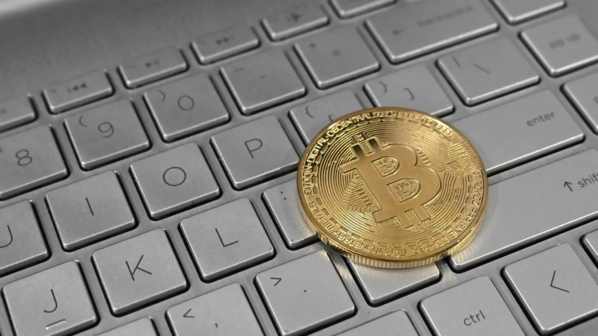 A physical bitcoin token resting on the keys of an open laptop computer, photographed close up from above