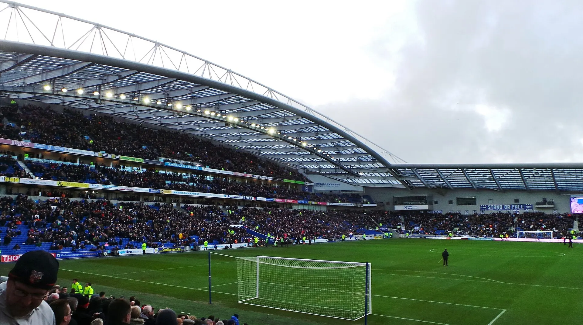 Brighton supporters fill the stands at the Amex Stadium in Falmer during a home Premier League match, with the pitch and a large club banner in view