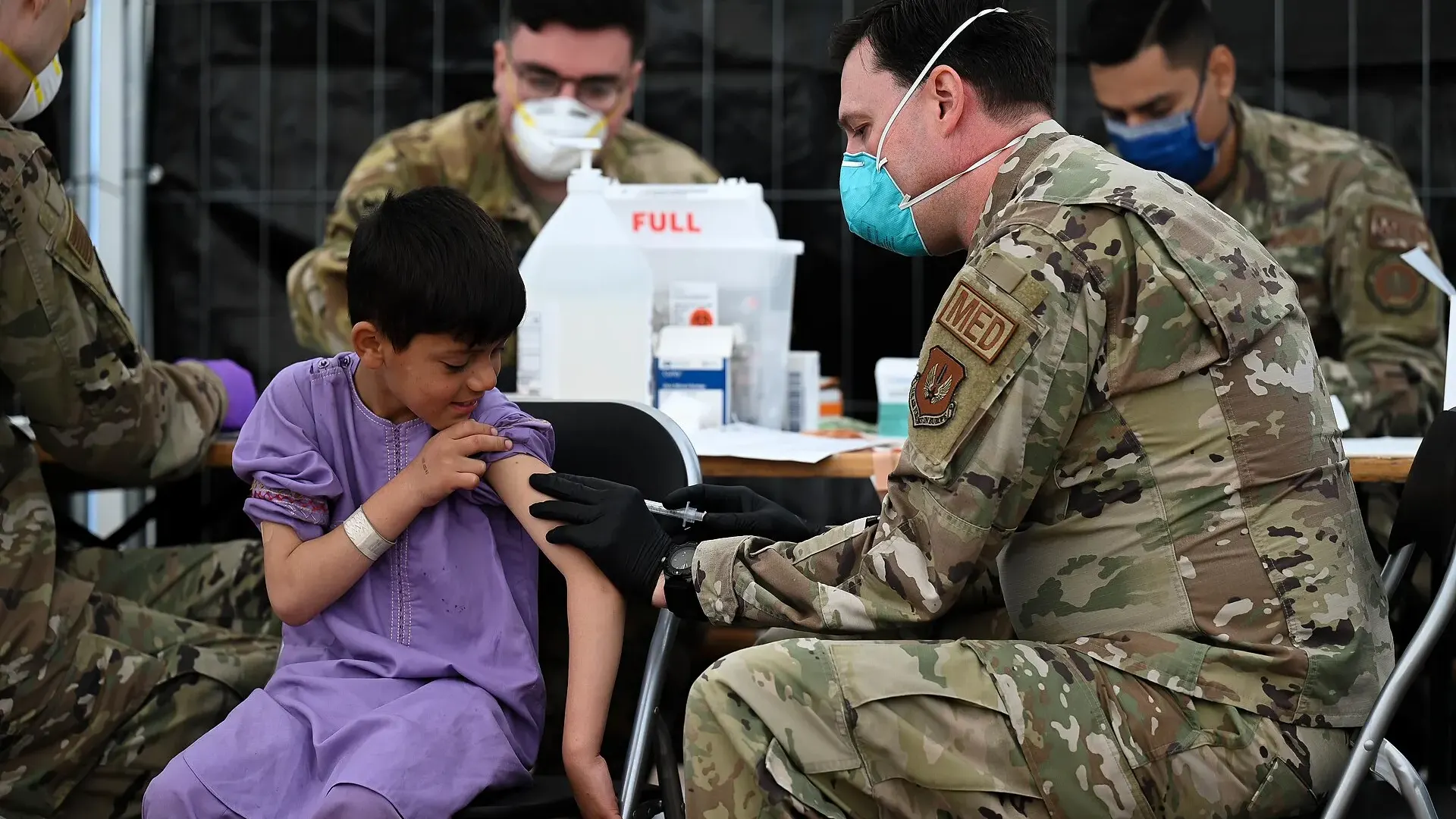 A U.S. Air Force medic in uniform gives a measles, mumps and rubella vaccine injection to a young child at Ramstein Air Base, Germany