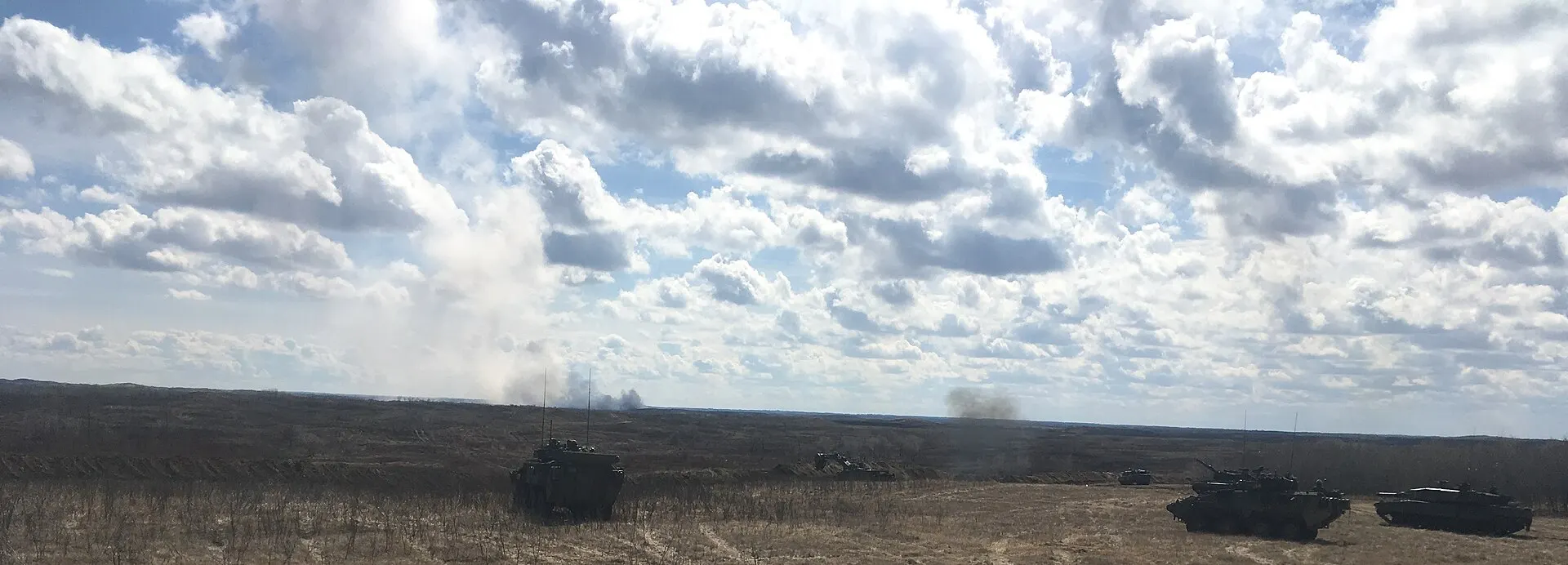 Canadian Army soldiers and armoured vehicles advance across open prairie grassland during a live-fire exercise at CFB Wainwright in Alberta.