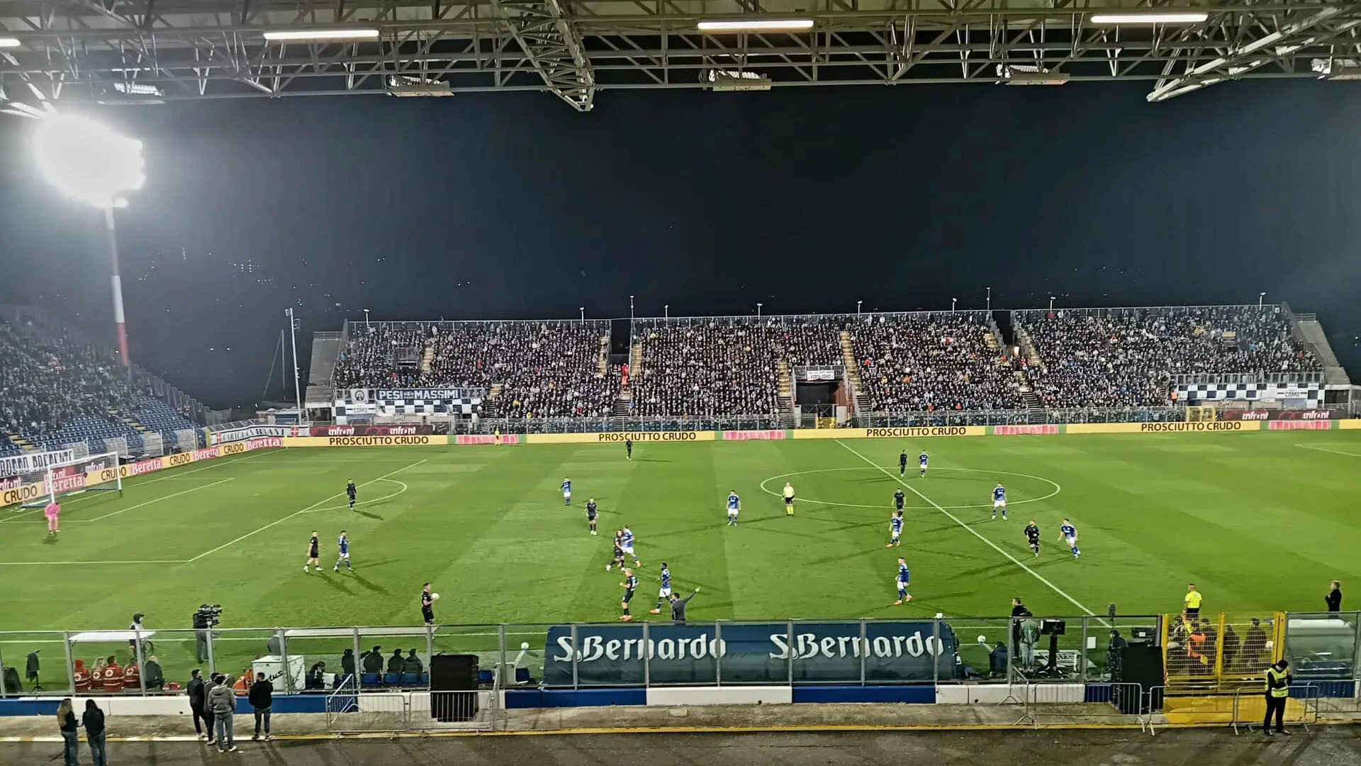 Players on the pitch at the Stadio Giuseppe Sinigaglia in Como during a Serie A match against Lazio in the 2024-25 season, with spectators in the stands