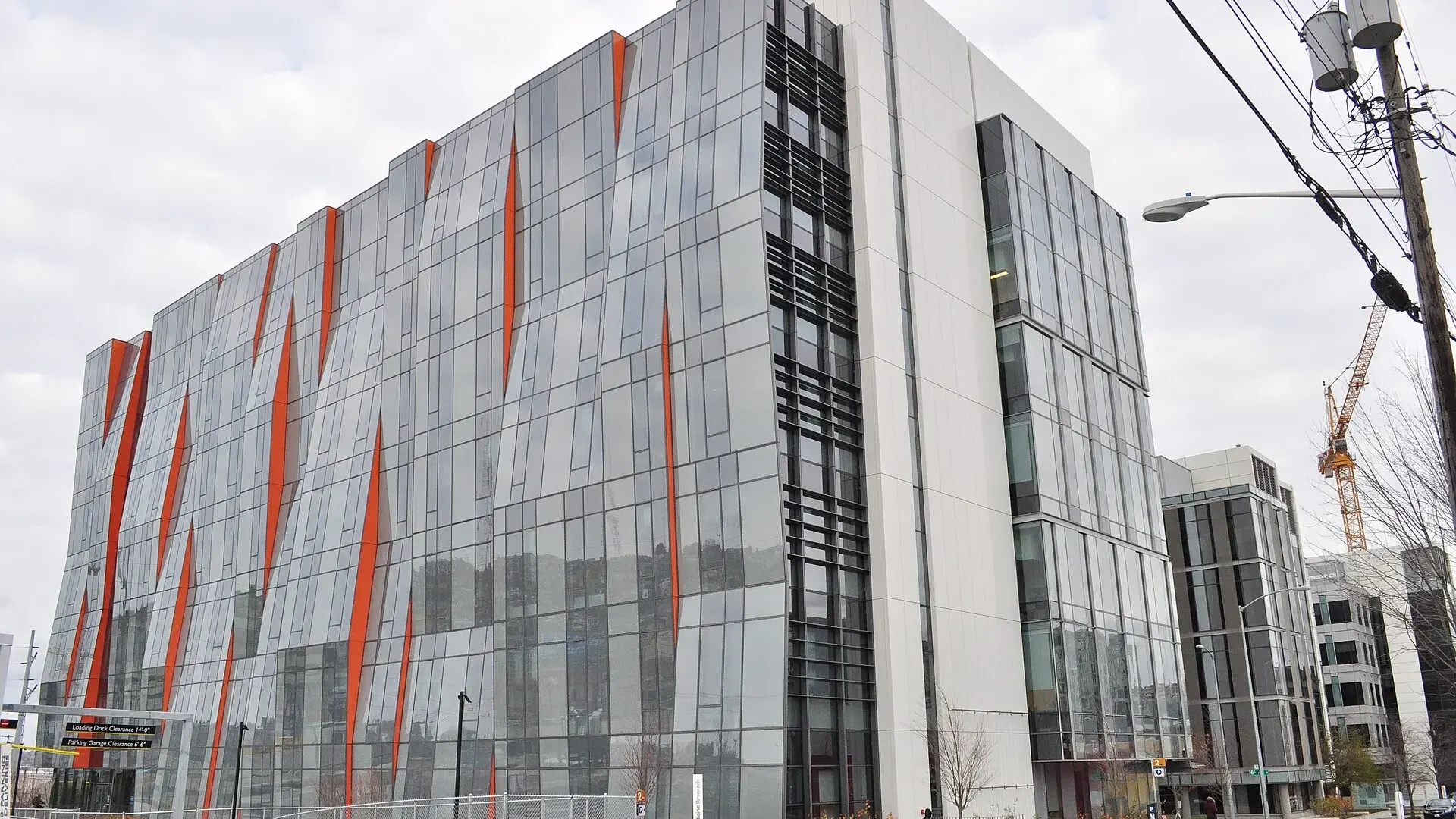 A glass-fronted UW Medicine Research building with orange accent panels in South Lake Union, Seattle, seen from street level under an overcast sky