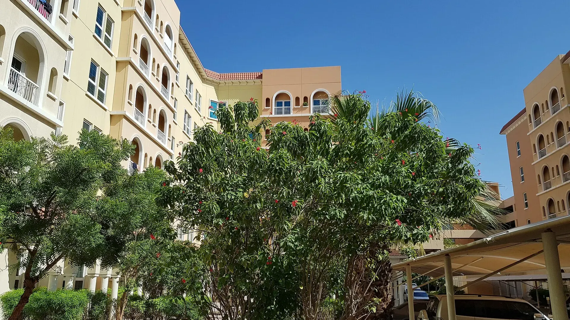 Low-rise residential apartment blocks with arched balconies, trees and a covered car park in Dubai Investments Park, Dubai
