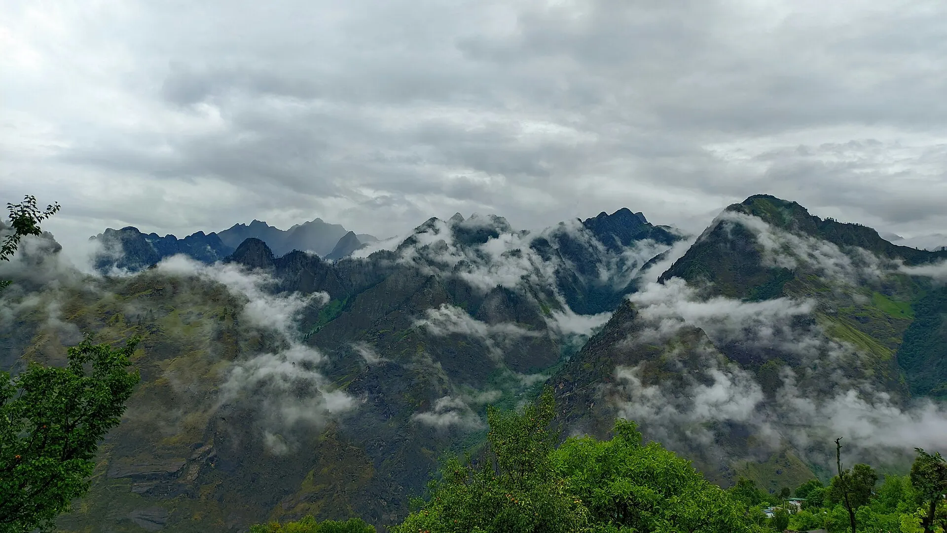 Cloud and mist hanging over snow-dusted Garhwal Himalayan peaks and forested ridges seen from the hill town of Joshimath in Uttarakhand