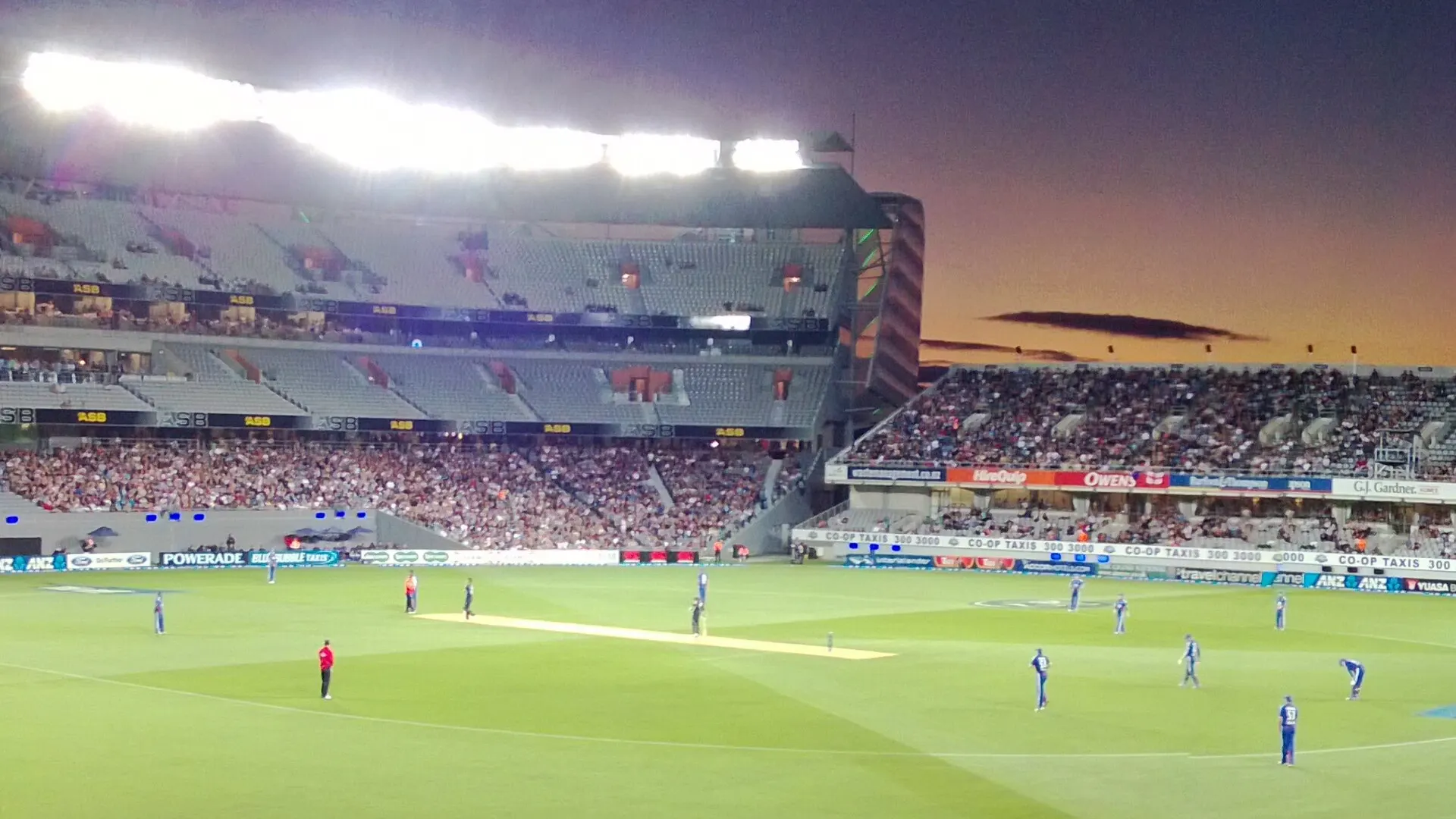 Eden Park in Auckland at dusk under floodlights during a Twenty20 cricket match, showing the south and west stands and the floodlit outfield