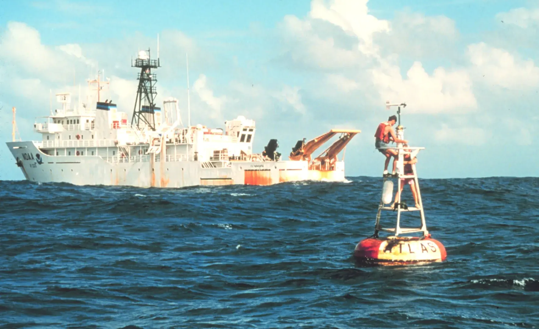 The NOAA research ship Ka'imimoana alongside an Atlas ocean buoy in the equatorial Pacific Ocean, with crew working on the buoy from the deck