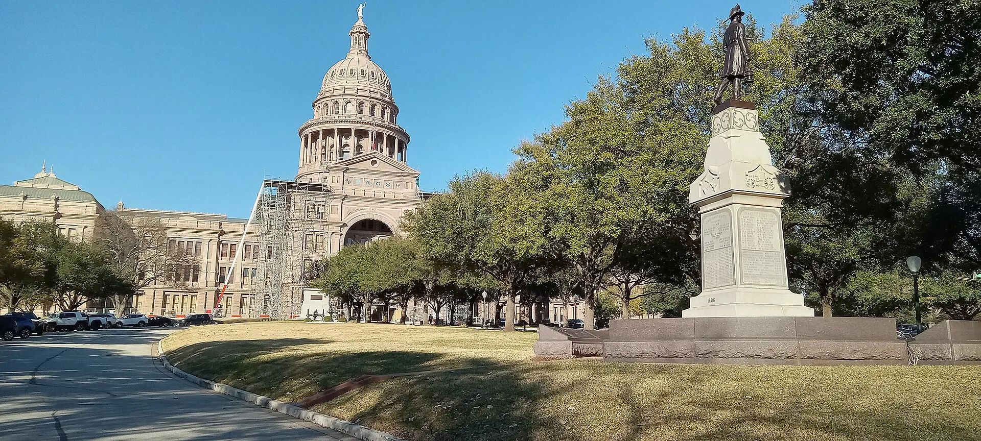 The pink granite dome of the Texas State Capitol in Austin rises behind trees and the Volunteer Firemen Monument in January 2023