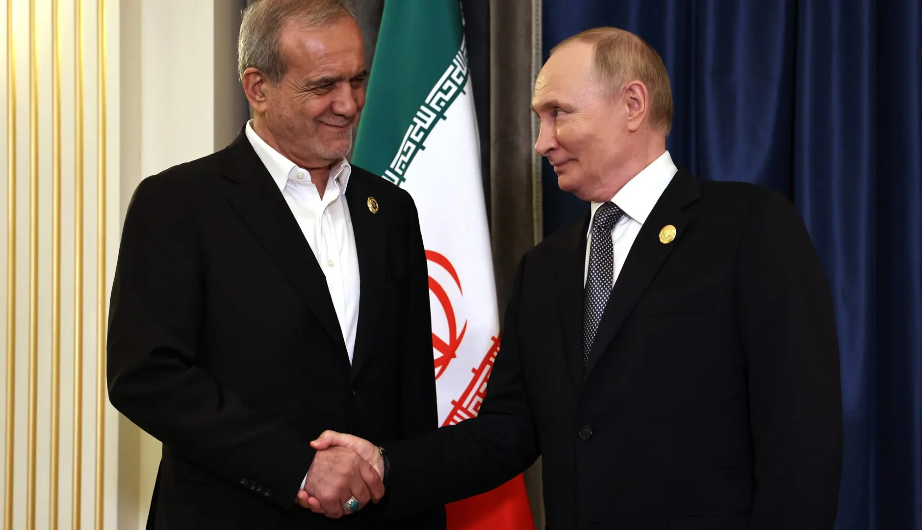 Iranian President Masoud Pezeshkian shakes hands with Russian President Vladimir Putin in front of an Iranian flag at a summit