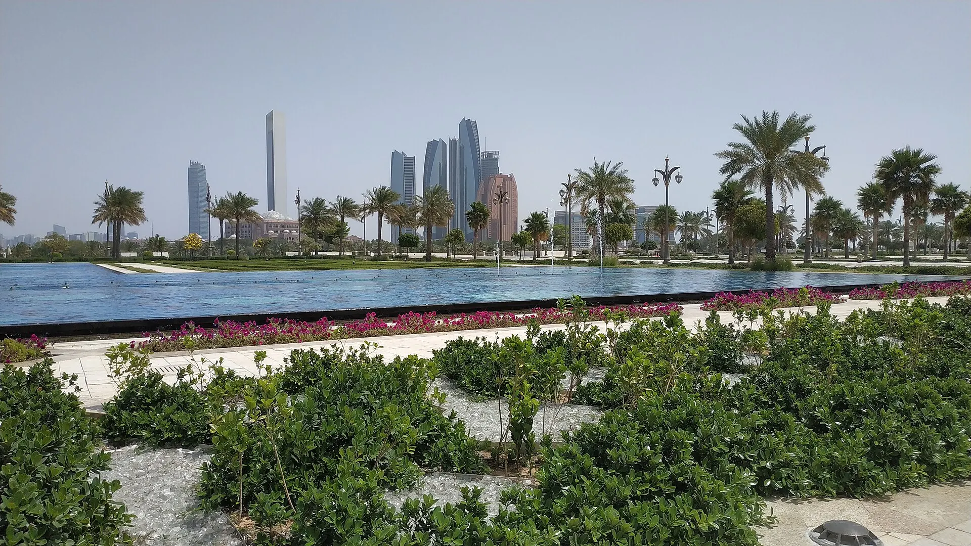 Gardens and a reflecting pool at Qasr Al Watan in Abu Dhabi, with palm trees and the Etihad Towers skyline behind