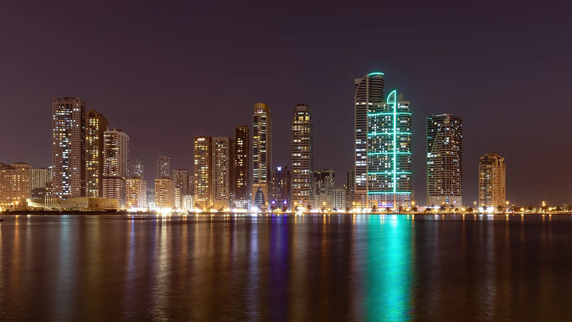 High-rise towers along the Sharjah waterfront seen across the water from near the Al Noor Mosque under a clear sky