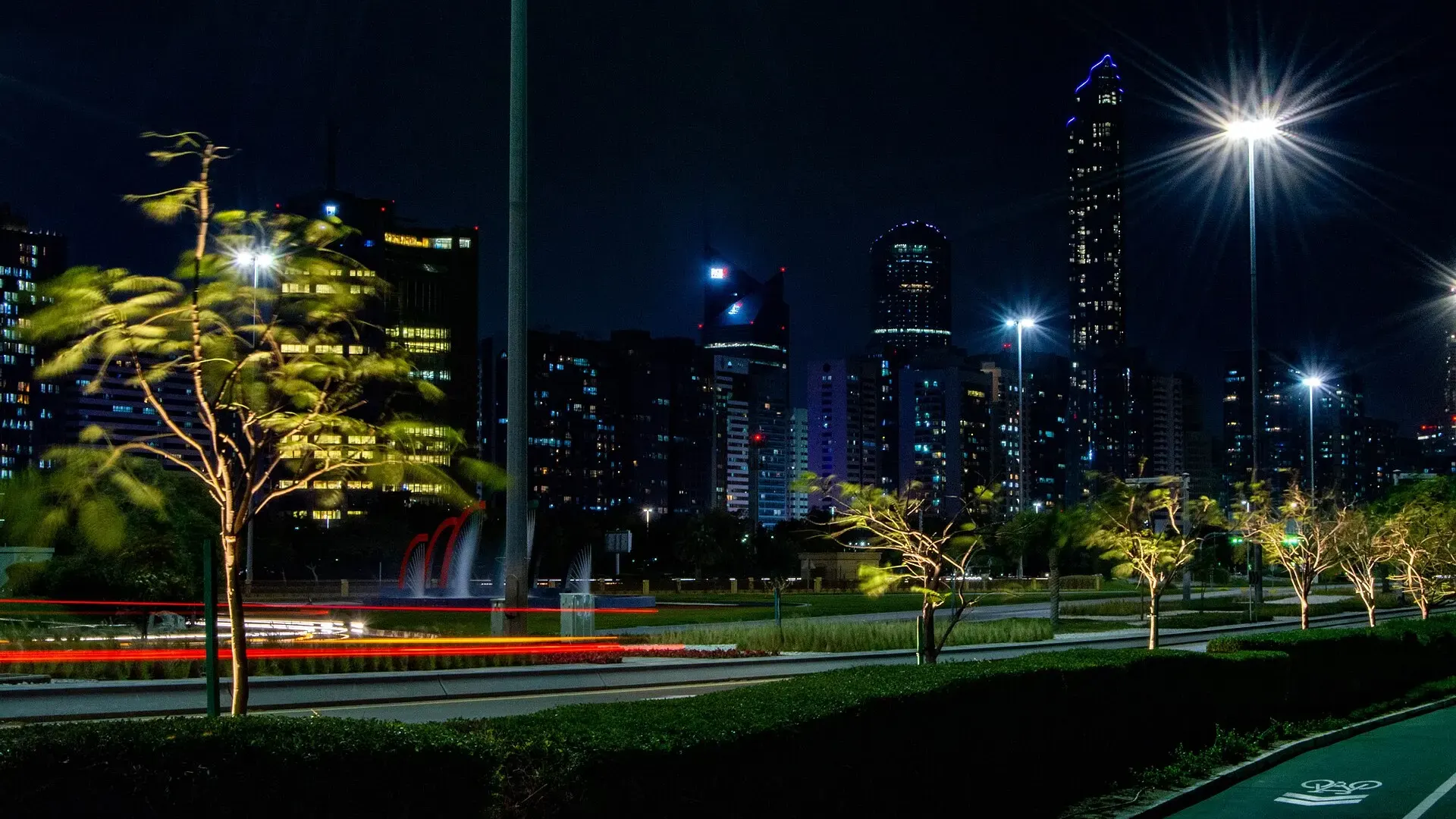 Abu Dhabi skyline at night seen from the Corniche, with lit office towers, a fountain and a bicycle lane in the foreground