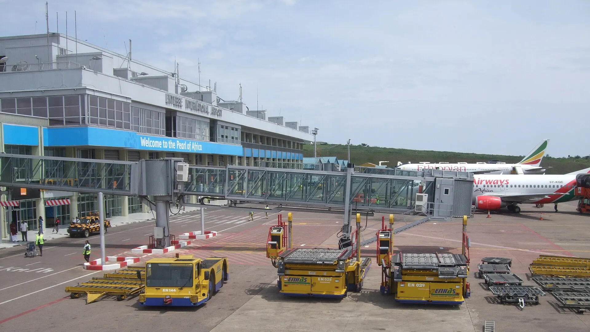 Entebbe International Airport terminal in Uganda with an Ethiopian Airlines jet and a Kenya Airways jet at the gates and baggage loaders on the apron, 2009