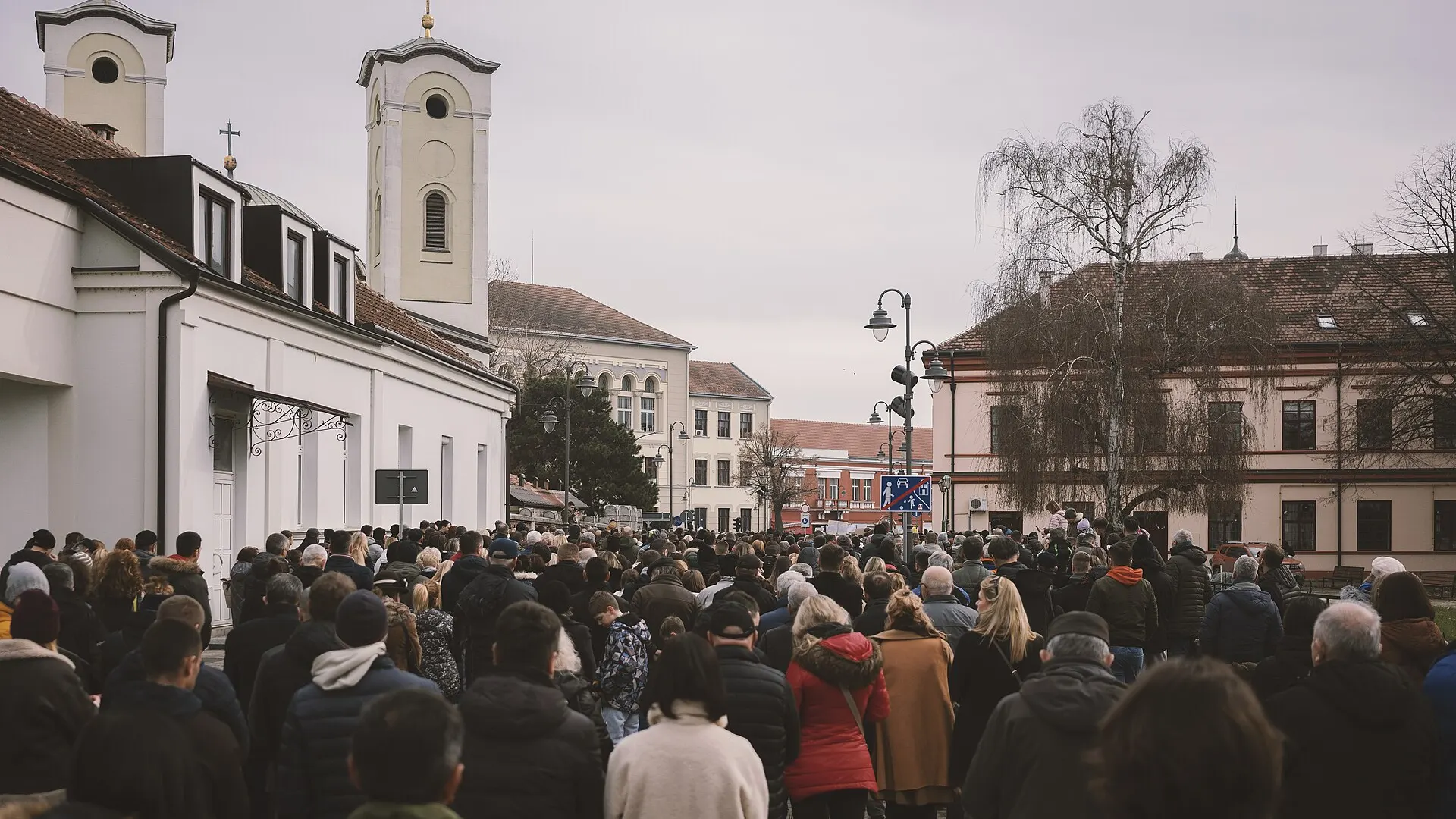 A crowd of protesters fills a street in Cacak, Serbia, in January 2025, many holding banners and Serbian flags.